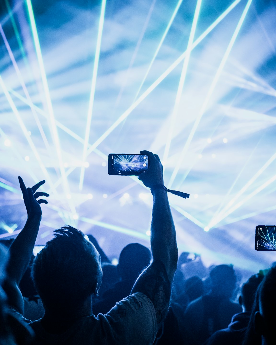 I partecipanti al concerto tengono i telefoni alzati verso il palco con luci laser.
